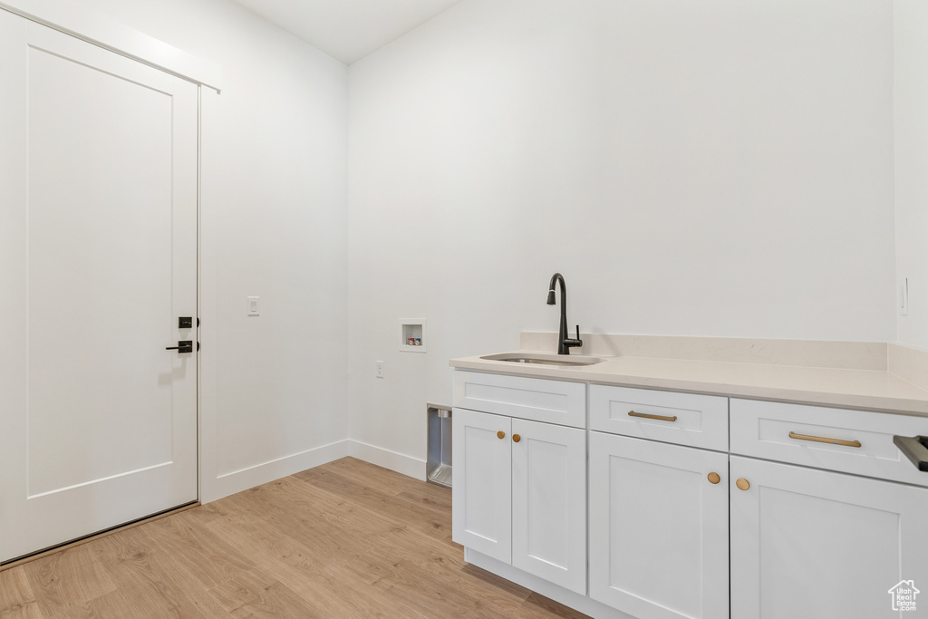 Washroom with light wood-style floors, baseboards, cabinet space, a sink, and washer hookup