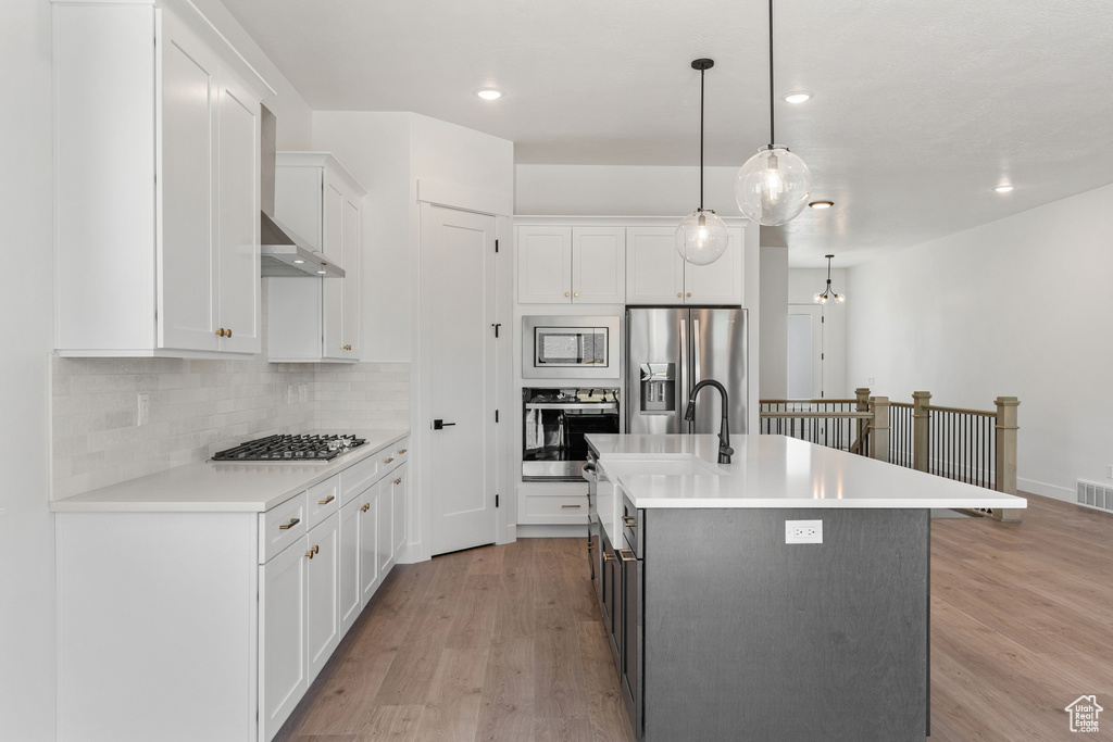 Kitchen with backsplash, appliances with stainless steel finishes, light wood-style flooring, and light countertops