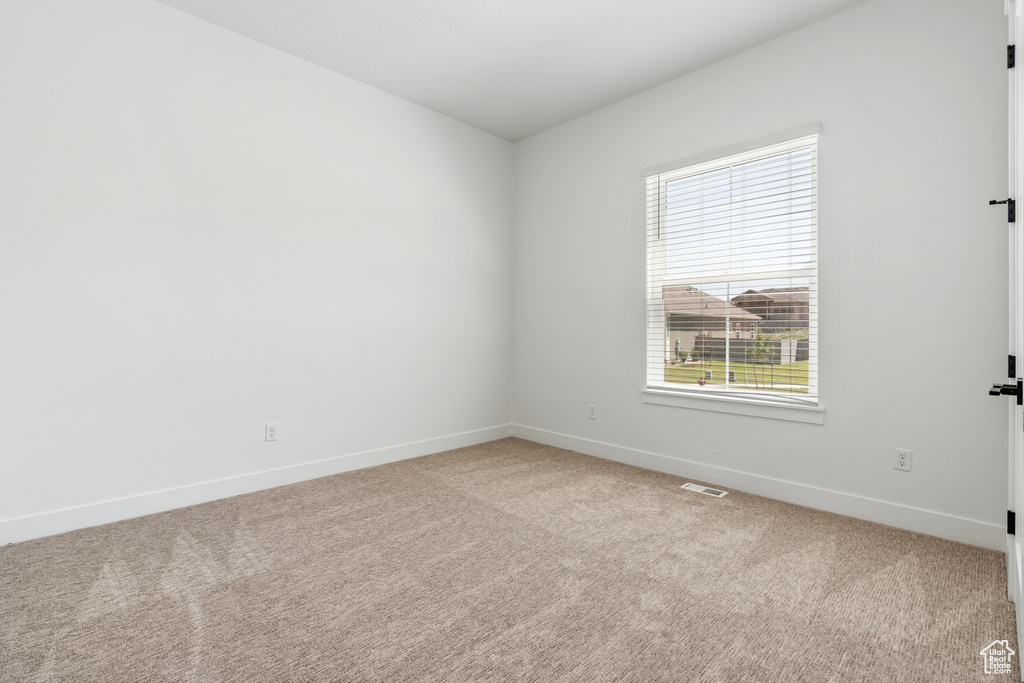 Carpeted spare room featuring baseboards, a healthy amount of sunlight, and visible vents
