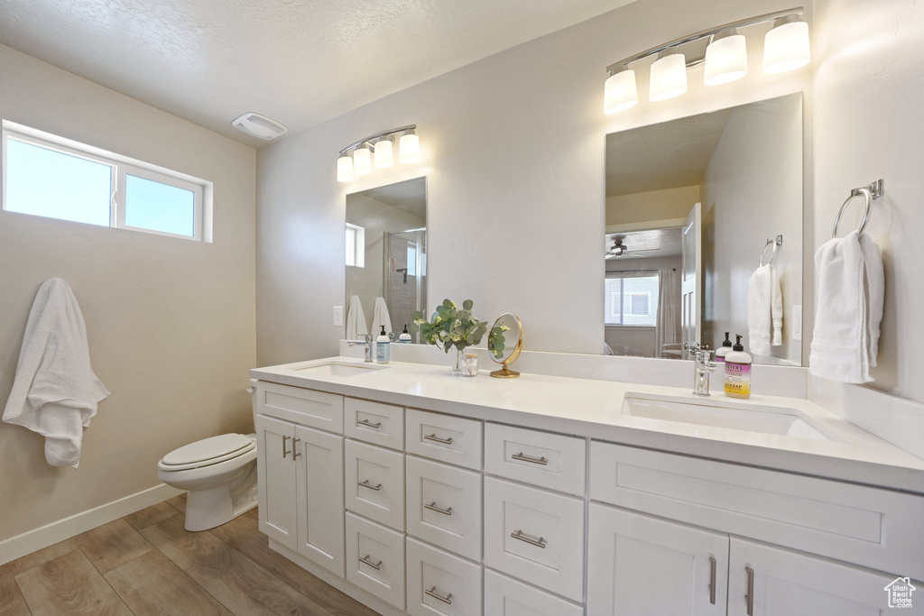 Bathroom featuring double vanity, a stall shower, wood finished floors, a sink, and toilet