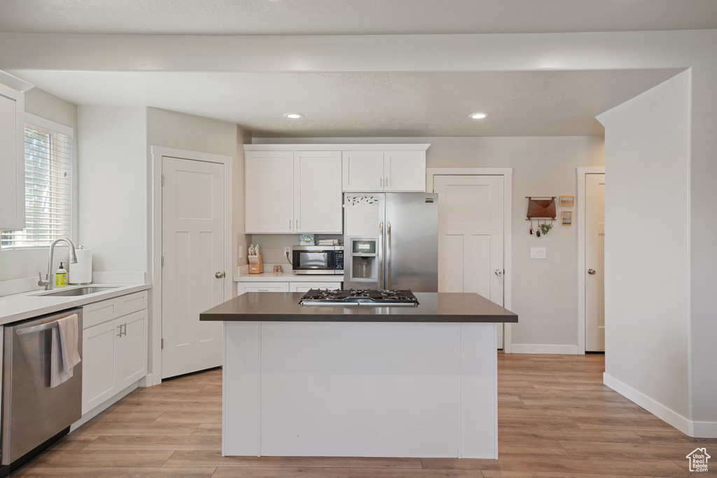 Kitchen with white cabinets, a sink, light wood-style flooring, a center island, and stainless steel appliances