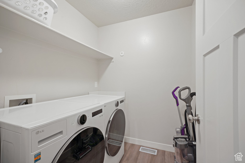 Laundry area with laundry area, light wood-style floors, baseboards, washer and clothes dryer, and a textured ceiling