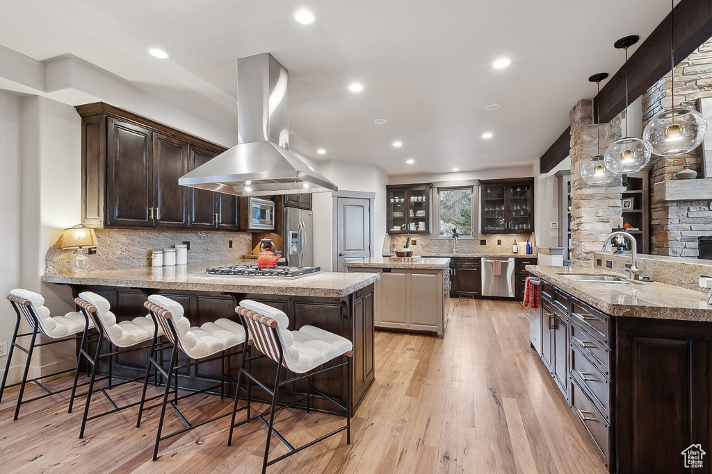 Kitchen featuring island exhaust hood, appliances with stainless steel finishes, a sink, a peninsula, and glass insert cabinets