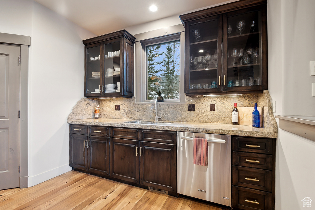 Bar with decorative backsplash, stainless steel dishwasher, light wood-type flooring, a sink, and baseboards