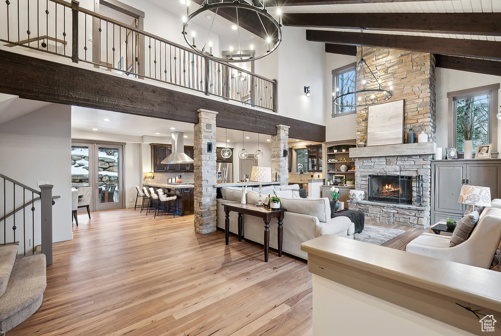 Living room featuring a stone fireplace, beam ceiling, wood finished floors, high vaulted ceiling, and a chandelier
