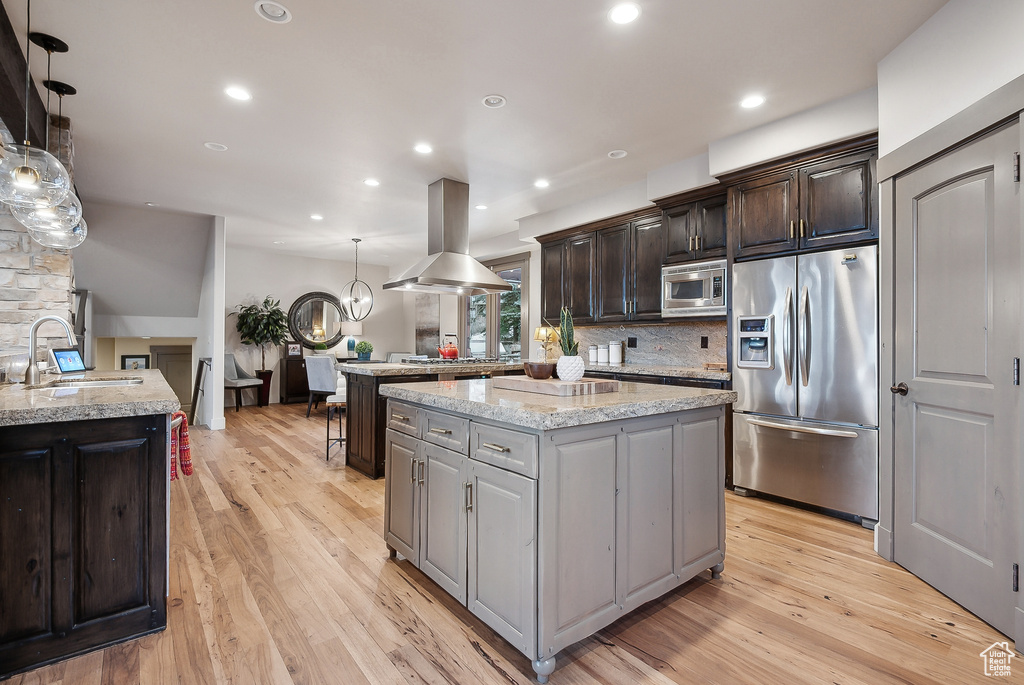 Kitchen featuring a kitchen island, island exhaust hood, a sink, light wood finished floors, and appliances with stainless steel finishes
