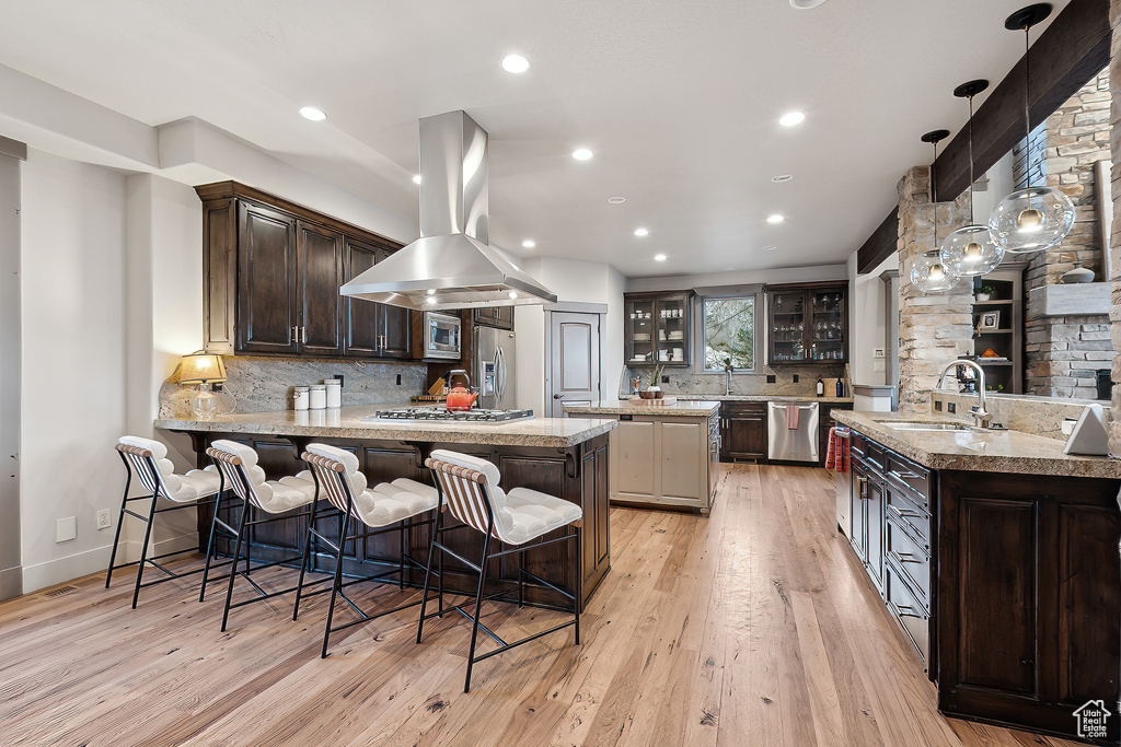 Kitchen featuring a sink, light wood-style flooring, stainless steel appliances, island exhaust hood, and glass insert cabinets