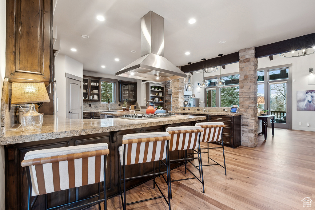 Kitchen with glass insert cabinets, island range hood, light wood finished floors, a peninsula, and stainless steel gas stovetop
