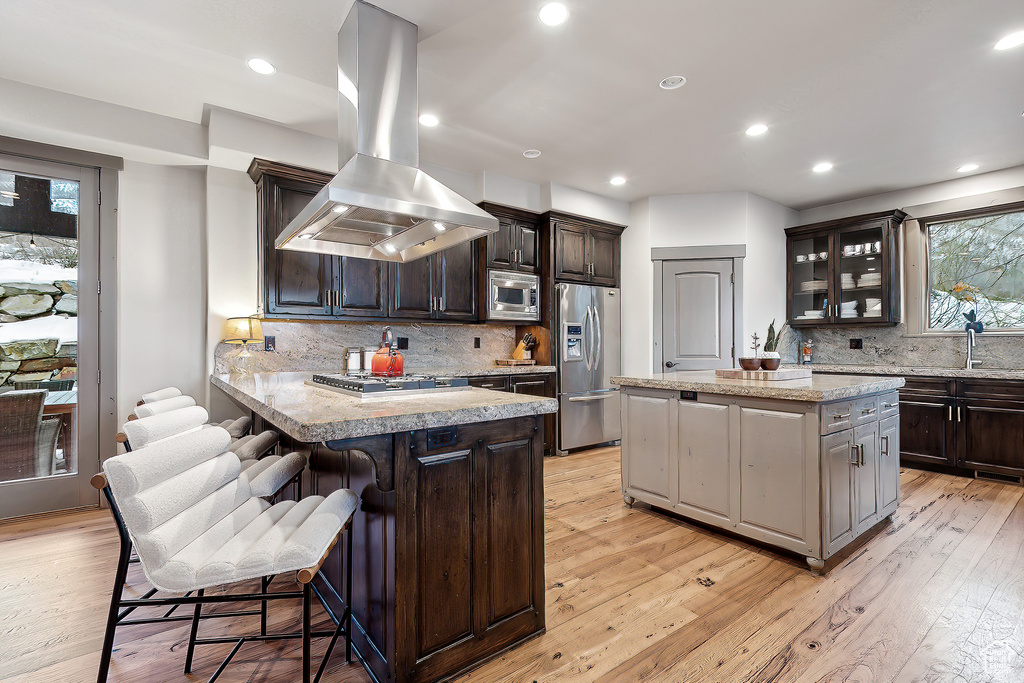 Kitchen with a kitchen breakfast bar, backsplash, island range hood, light countertops, and stainless steel appliances