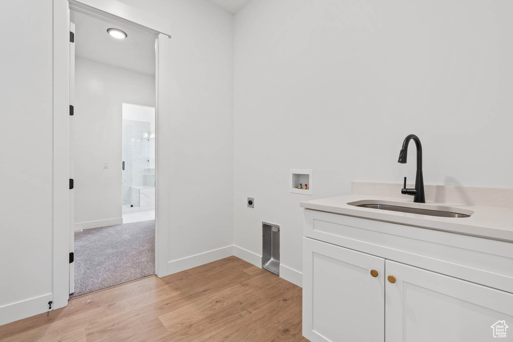 Laundry room with cabinet space, a sink, light wood finished floors, hookup for a washing machine, and electric dryer hookup