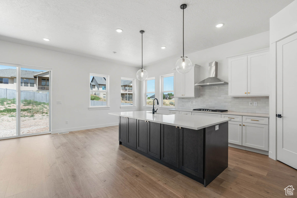 Kitchen with a sink, wall chimney exhaust hood, white cabinets, and light countertops