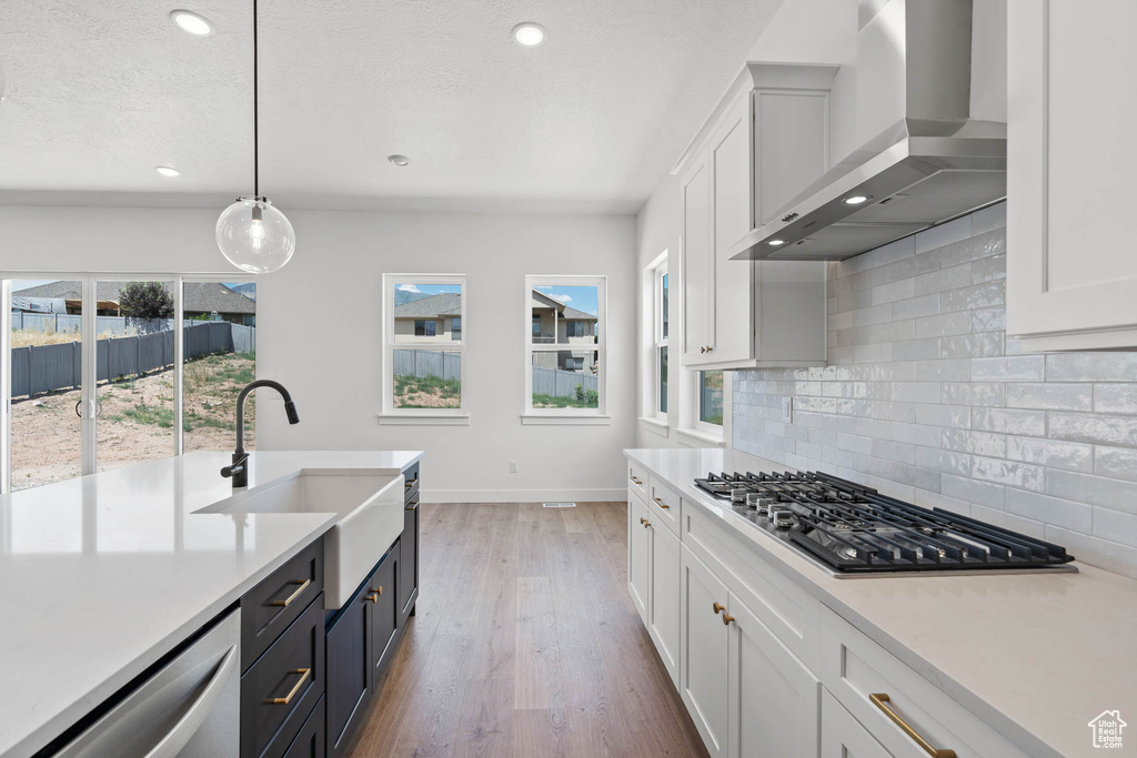 Kitchen with wall chimney range hood, white cabinets, appliances with stainless steel finishes, light countertops, and baseboards