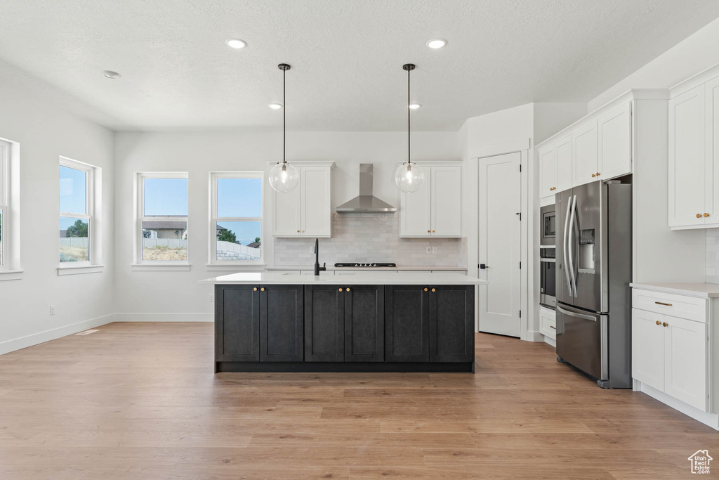 Kitchen with light countertops, wall chimney exhaust hood, appliances with stainless steel finishes, and white cabinetry