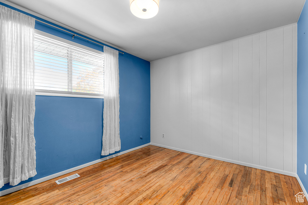 Empty room with wood-type flooring, baseboards, and visible vents