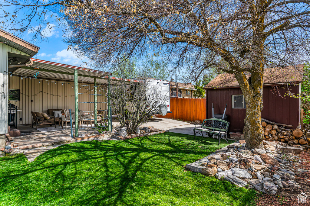 View of yard with fence, an outdoor structure, a patio area, and a shed