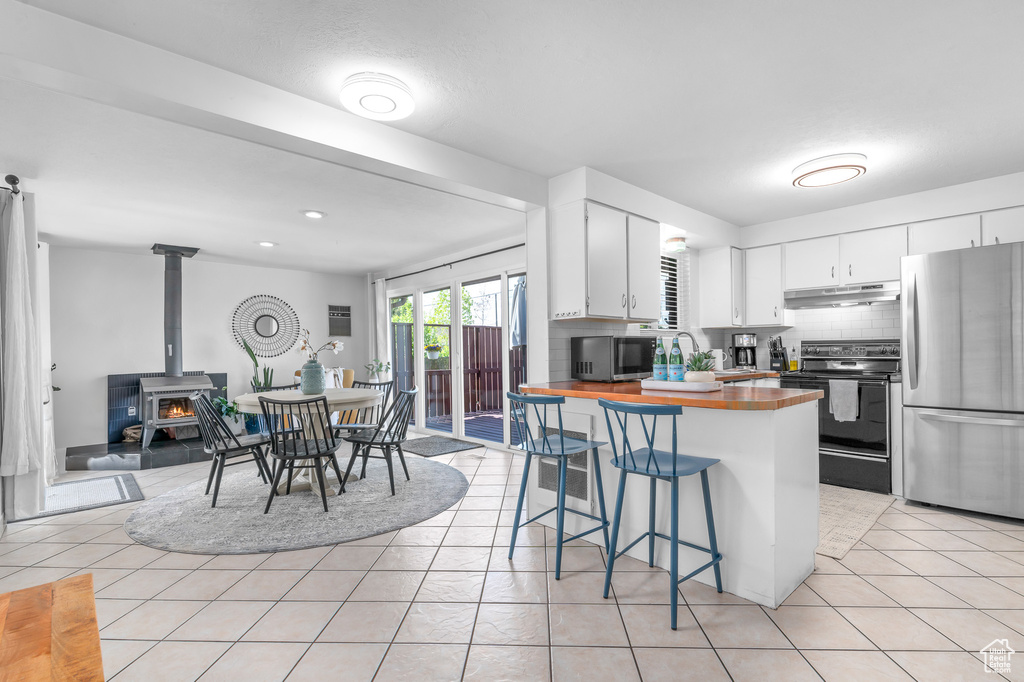 Kitchen with appliances with stainless steel finishes, a kitchen breakfast bar, butcher block countertops, tasteful backsplash, and under cabinet range hood