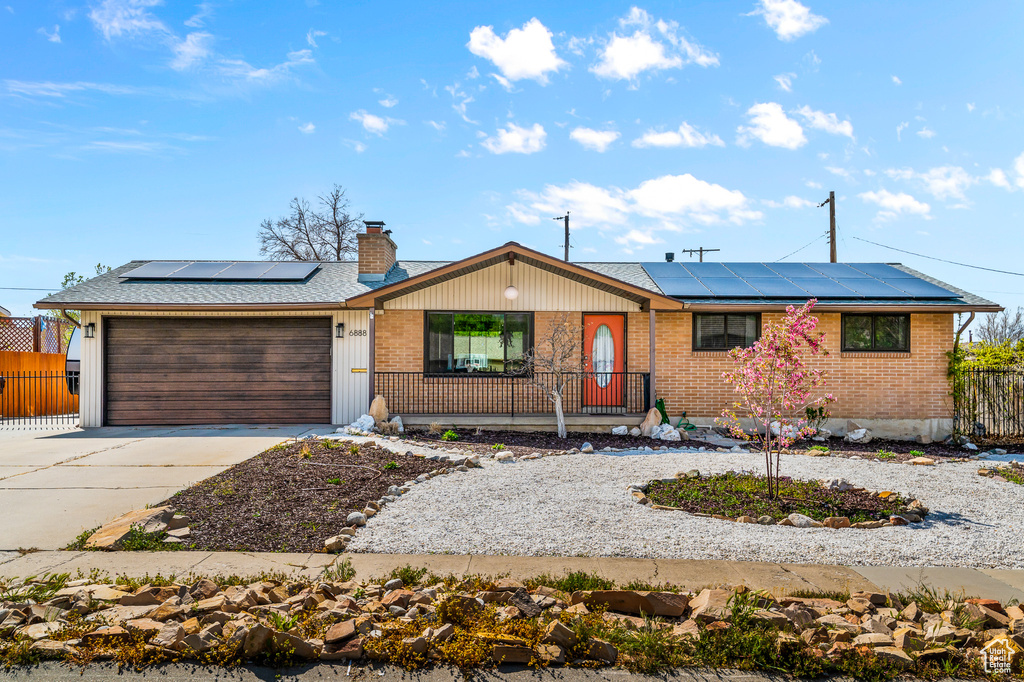 Ranch-style house with roof mounted solar panels, an attached garage, driveway, and brick siding