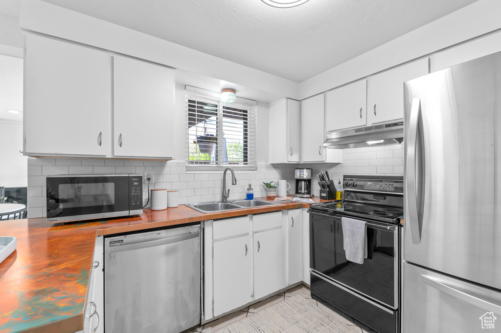 Kitchen with a sink, wood counters, backsplash, under cabinet range hood, and black appliances