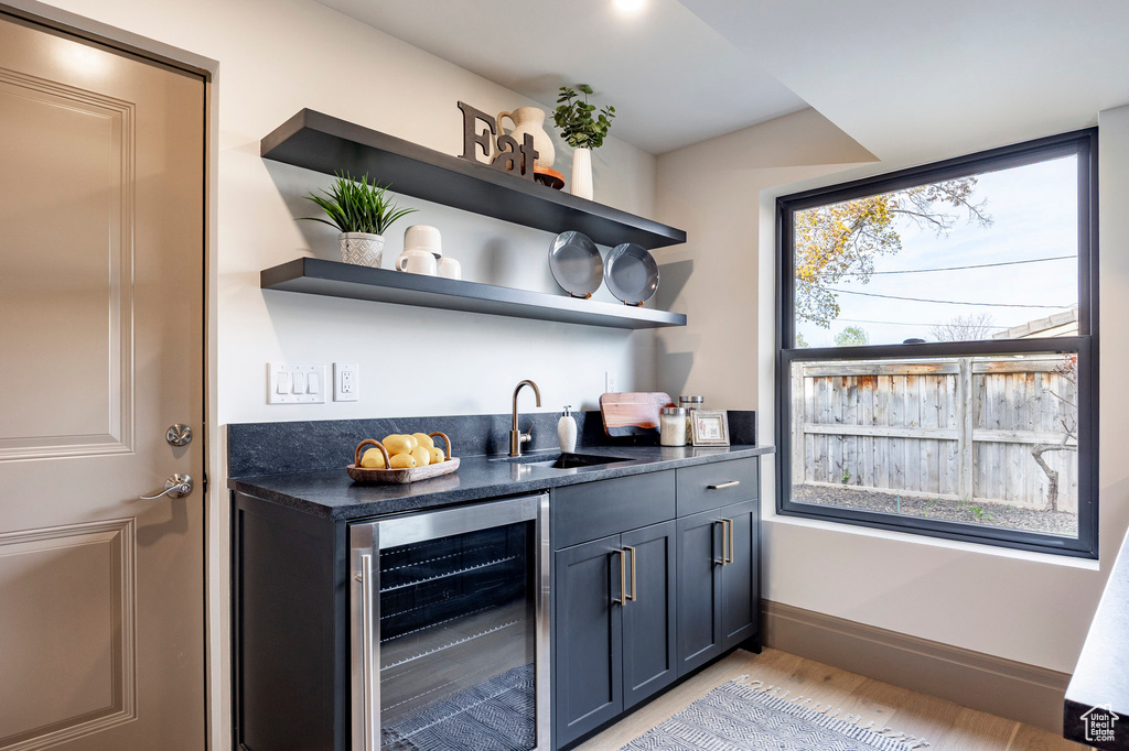 Bar featuring a sink, light wood-style floors, baseboards, wet bar, and wine cooler