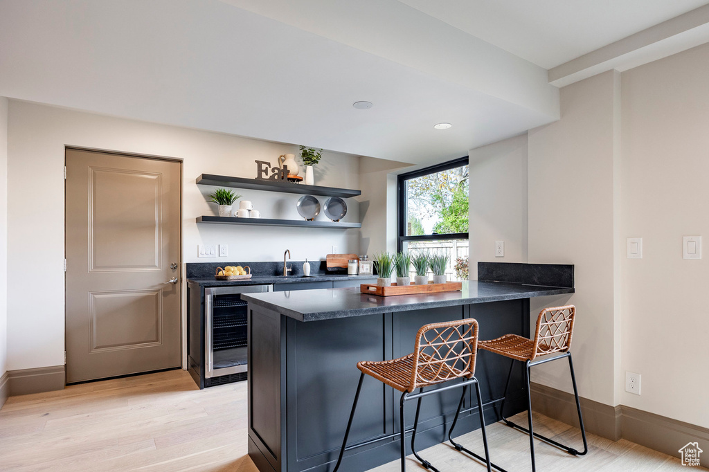 Bar featuring wine cooler, indoor wet bar, baseboards, a sink, and light wood-style flooring
