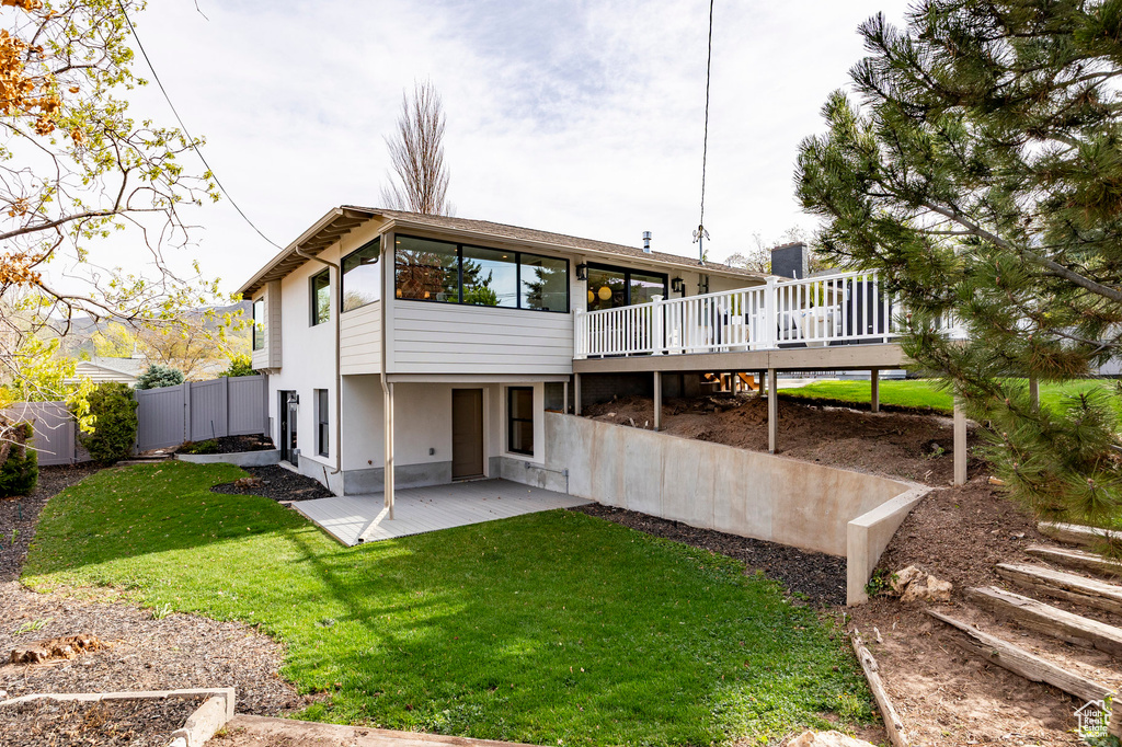 Rear view of property with a lawn, a wooden deck, a patio area, fence, and stucco siding