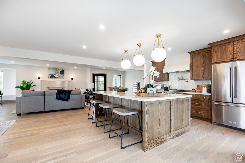 Kitchen with a spacious island, custom exhaust hood, high quality fridge, and light wood-style flooring