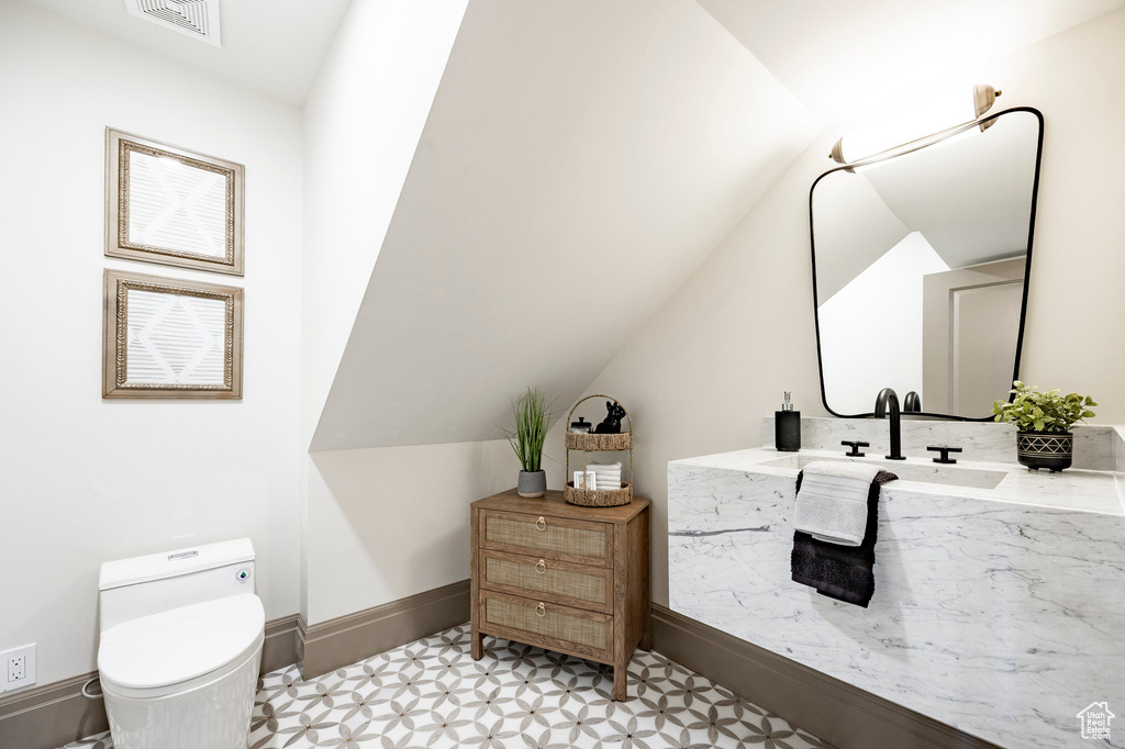 Half bath featuring toilet, tile patterned floors, baseboards, lofted ceiling, and visible vents