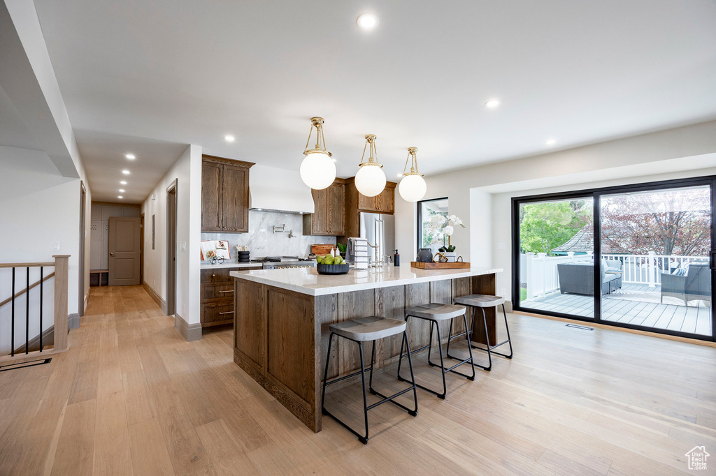Kitchen with custom exhaust hood, a spacious island, light countertops, light wood finished floors, and backsplash
