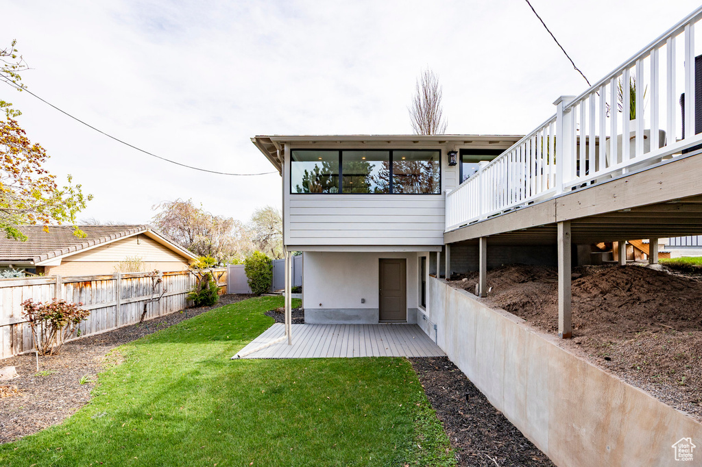Back of property featuring a fenced backyard, a wooden deck, a lawn, and a patio area