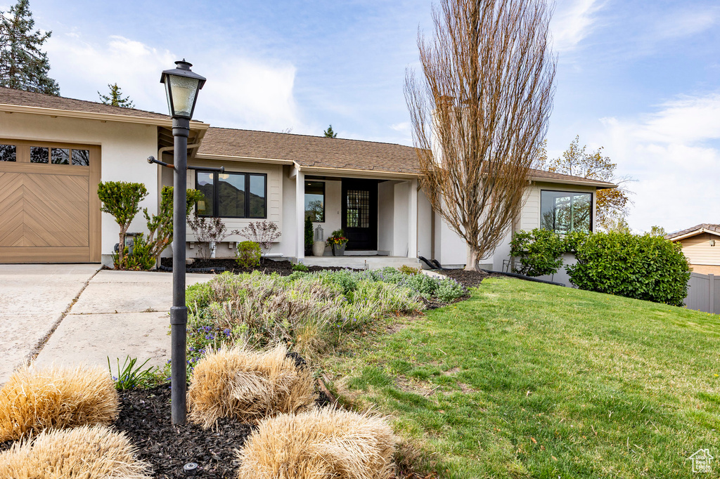 Ranch-style home with a garage, a front lawn, stucco siding, a porch, and driveway