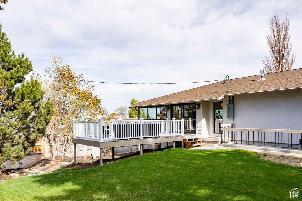 Rear view of house featuring a lawn, a wooden deck, stucco siding, and roof with shingles