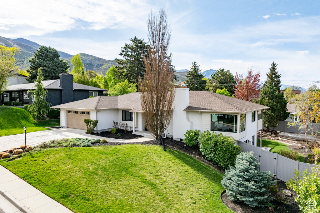 View of front of property with fence, a front lawn, a garage, a mountain view, and concrete driveway