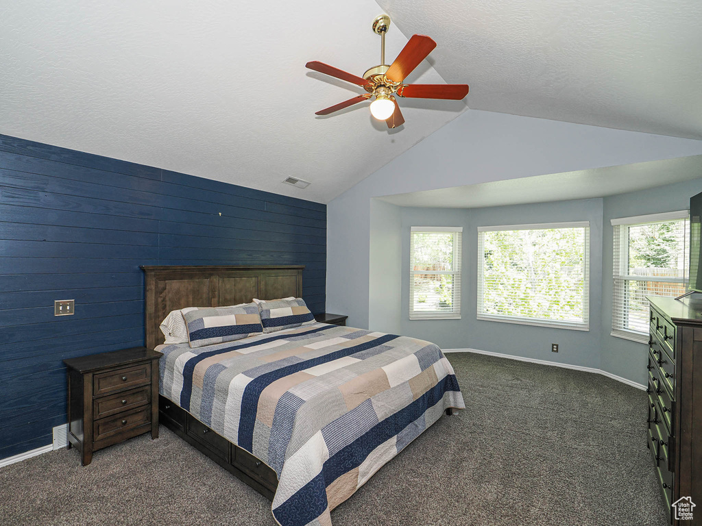 Bedroom with wood walls, vaulted ceiling, baseboards, and dark colored carpet