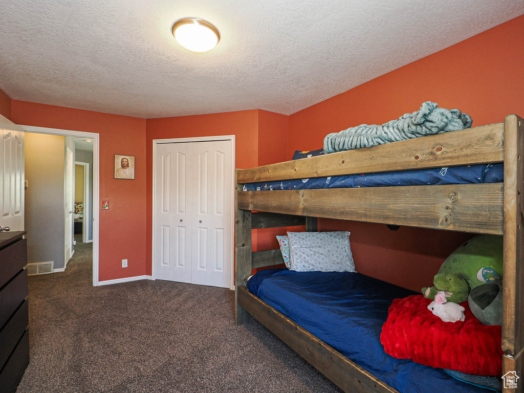 Carpeted bedroom with a closet, a textured ceiling, and baseboards