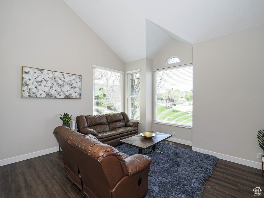 Living room with dark wood-style flooring, baseboards, and high vaulted ceiling