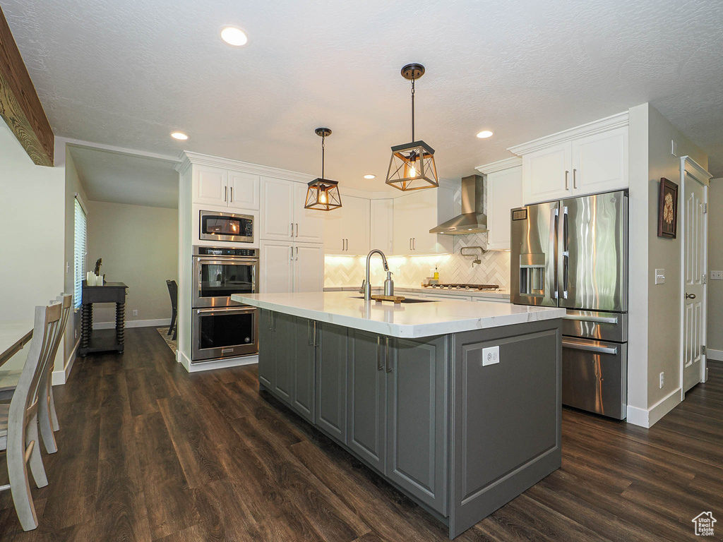 Kitchen featuring a sink, wall chimney exhaust hood, stainless steel appliances, baseboards, and gray cabinetry