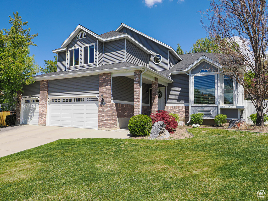 View of front facade with roof with shingles, brick siding, a garage, a front yard, and driveway