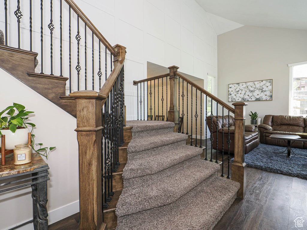 Stairs featuring baseboards, wood finished floors, and high vaulted ceiling