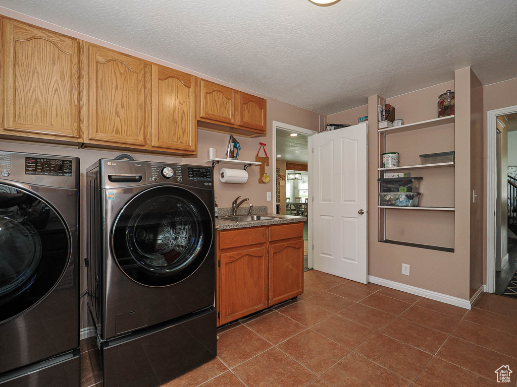 Washroom featuring cabinet space, a textured ceiling, washing machine and dryer, and a sink