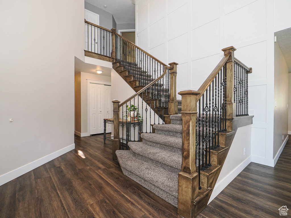 Staircase featuring baseboards, wood finished floors, and a high ceiling