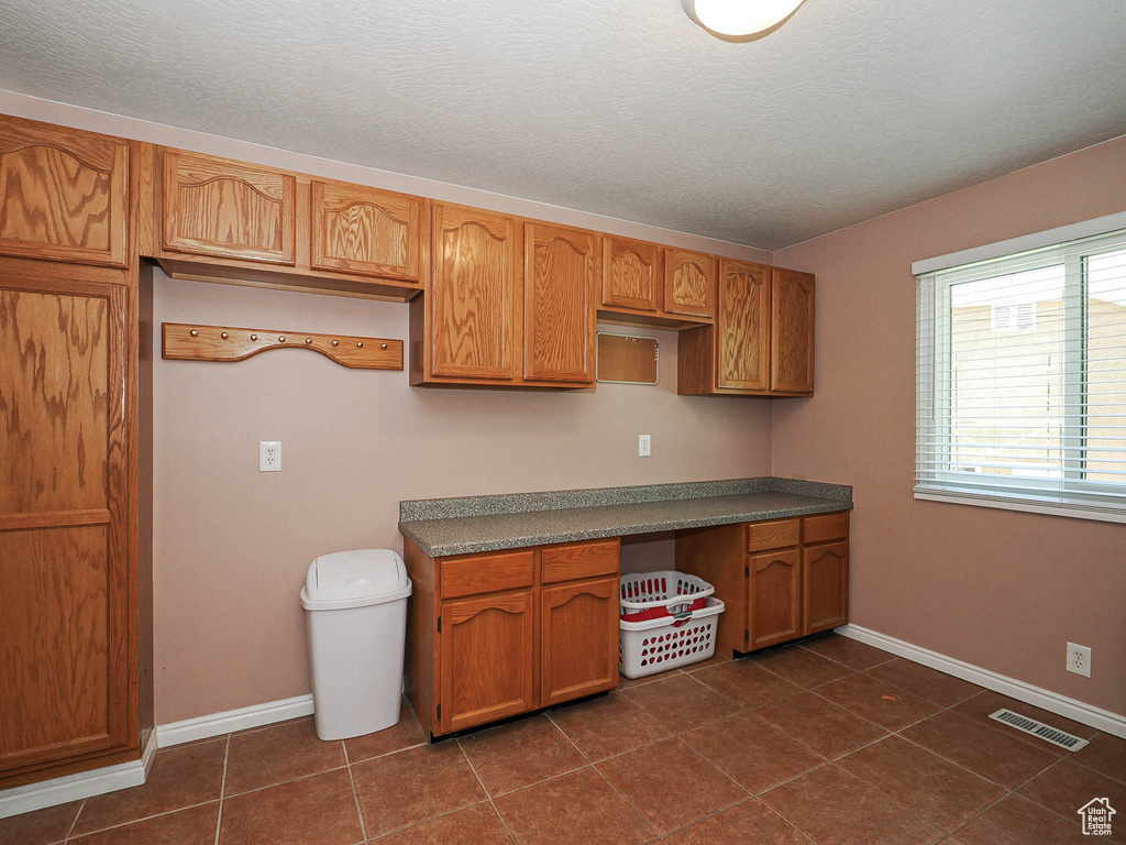 Kitchen with visible vents, baseboards, dark tile patterned floors, a textured ceiling, and brown cabinets