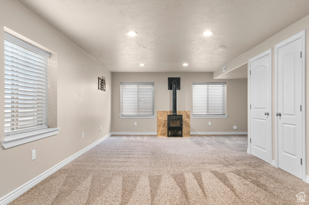 Unfurnished living room with carpet flooring, recessed lighting, baseboards, and a wood stove