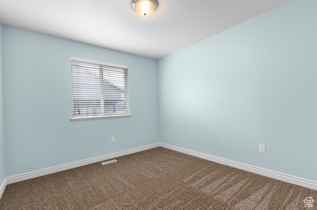 Carpeted spare room featuring visible vents and baseboards