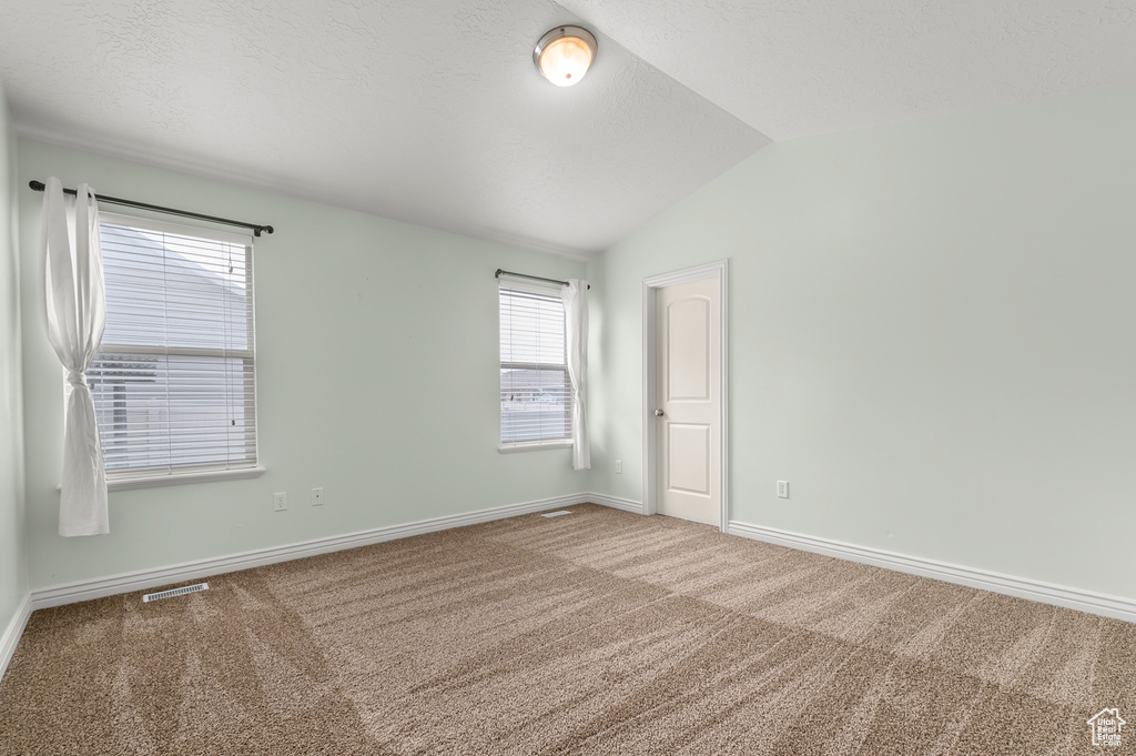 Empty room featuring visible vents, carpet, baseboards, and vaulted ceiling
