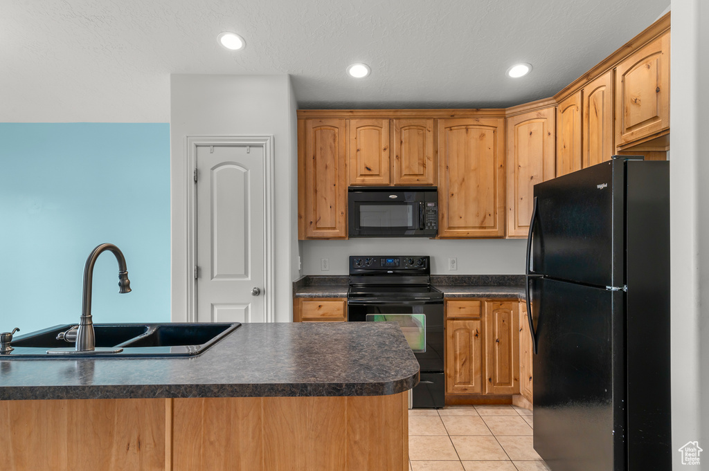 Kitchen featuring a sink, dark countertops, black appliances, and light tile patterned flooring