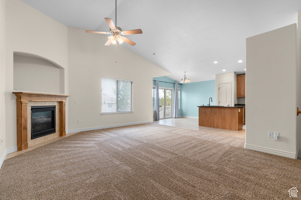 Unfurnished living room with baseboards, light colored carpet, recessed lighting, a tile fireplace, and ceiling fan with notable chandelier