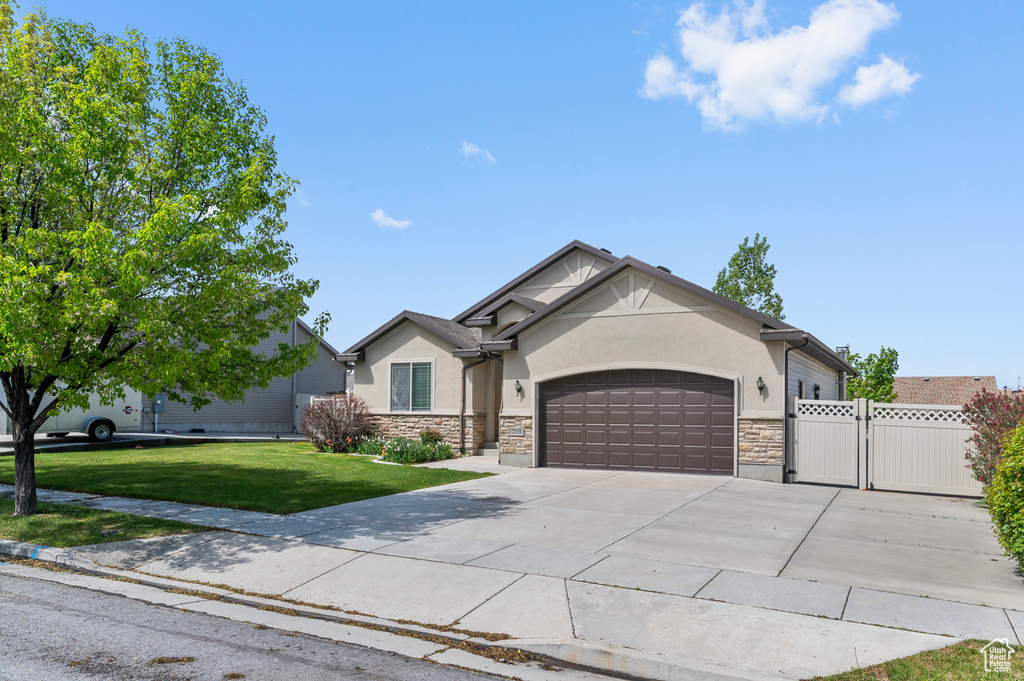 View of front facade featuring a front yard, a gate, a garage, stone siding, and stucco siding