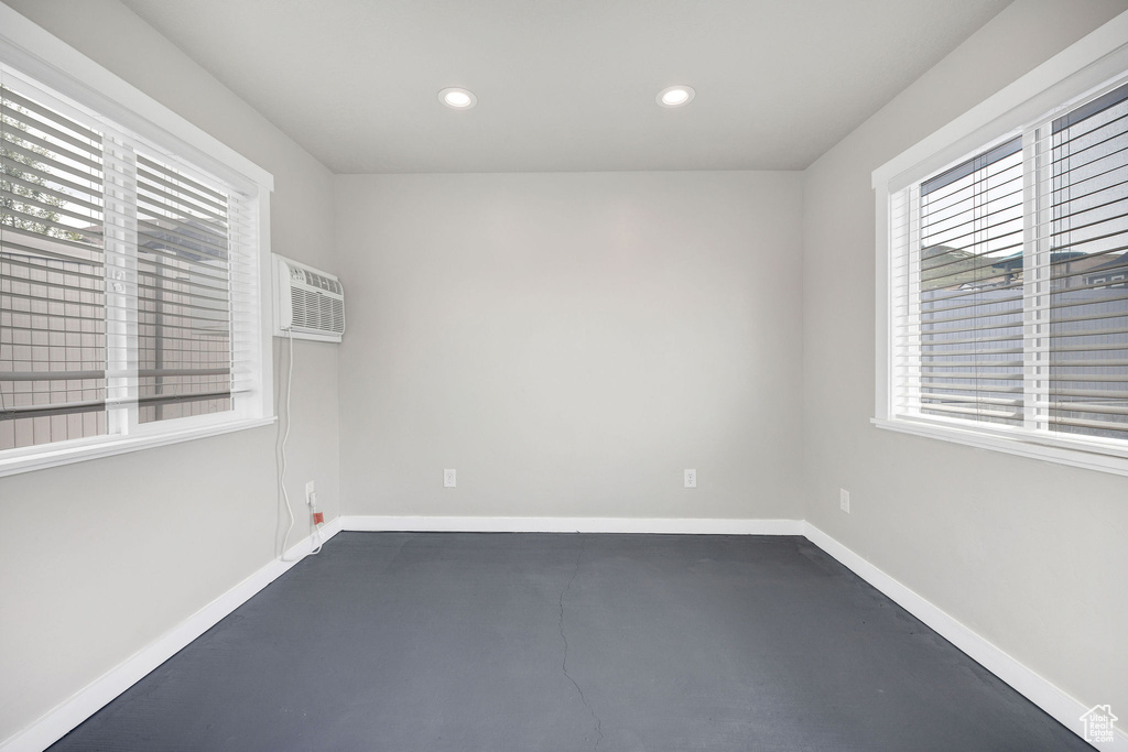 Unfurnished room featuring baseboards, a wall mounted AC, concrete flooring, and recessed lighting