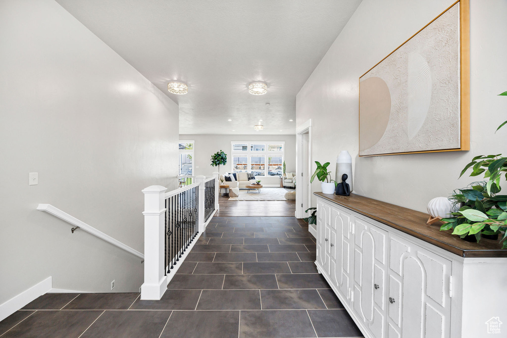 Corridor featuring dark tile patterned floors, baseboards, and an upstairs landing
