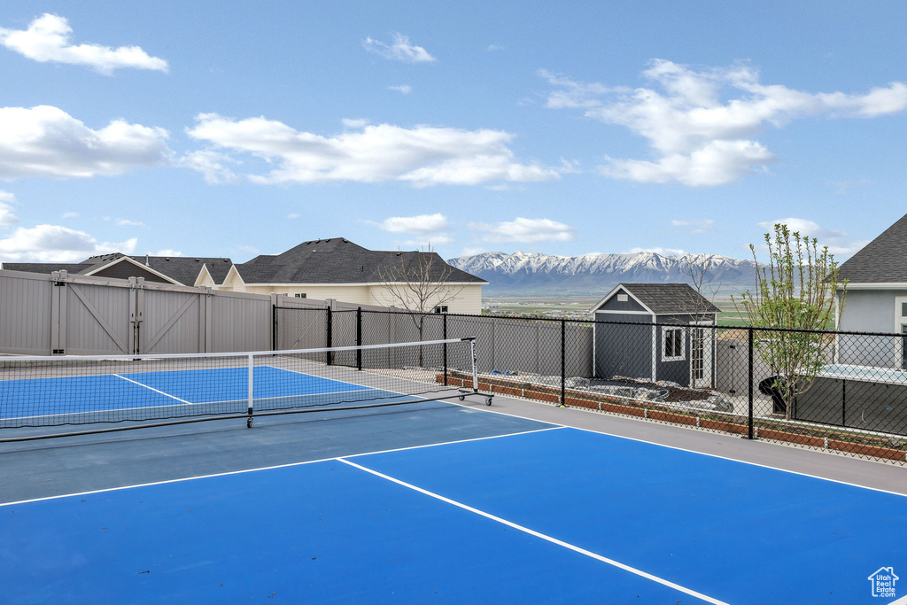View of sport court with fence, a mountain view, an outbuilding, and a storage shed